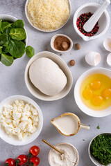 Dough, crumbled feta cheese, raw eggs broken into a bowl, grated Parmesan cheese, cream, spinach, herbs and spices prepared for baking quiche Lorraine pie.