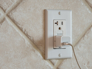 USB cell phone power adapter brick and cord in GFCI wall plug. Electrical cord and charger plug in...