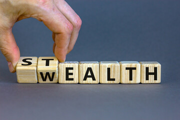 Stealth wealth symbol. Businessman turns wooden cubes and changes the word 'wealth' to 'stealth'....