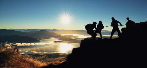 Young asian couple hikers climbing up on the peak of mountain. People helping each other hike up a mountain at sunrise. Giving a helping hand. Climbing. Helps and team work concept - obrazy, fototapety, plakaty
