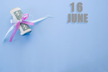 calendar date on blue background with rolled up dollar bills pinned by blue and pink ribbon with copy space. June 16 is the sixteenth day of the month