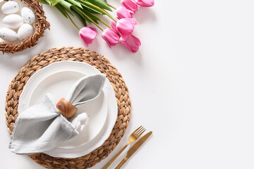 Easter dinner with eggs, bunny, festive tableware and tulips on white.