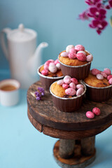 Muffins decorated with pink chocolate eggs. Easter muffin. Pink, blue, purple. Side view, blue background. Coffee, flowers.