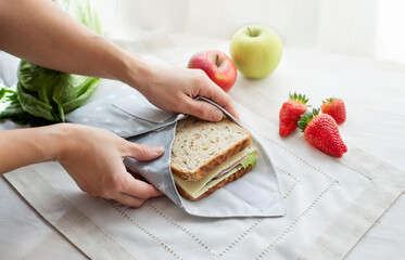 Person hands wrapping whole grain sandwich wrapped in reusable bag. Zero waste ecologic concept