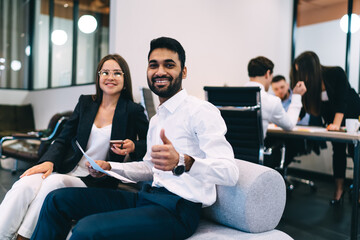Positive young multiracial business partners working in stylish office sitting on couch