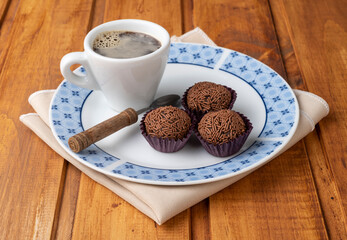 Typical brazilian brigadeiros on a plate with a cup of coffe over wooden table