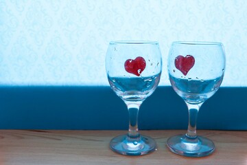 Two empty wine glasses with red hearts inside on blue background. Romantic night concept 