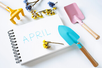 april written in notebook, flowers and colorful gardening tools