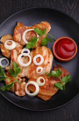 Grilled chicken fillet with tomato sauce and greens on a black background.