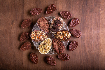 Top view of six mini stuffed easter eggs on a glass plate and mini crunchy stuffed chocolate with peanut easter eggs around it on a wooden table.