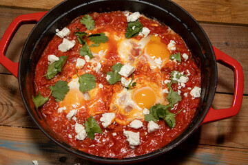 A delicious pot of Shakshuka with avocado and harissa eggs boiling in a large red cook pot
