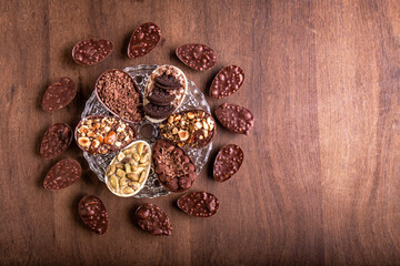 Top view of six mini stuffed easter eggs on a glass plate and mini crunchy stuffed chocolate with peanut easter eggs around it on a wooden table with free space on the right.