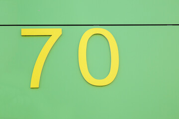 Yellow number seventy on a green house wall, background for a birthday template, no person
