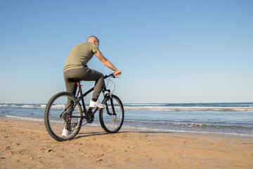 Obraz premium Boy with green shirt and mask arriving at his destination after a bike ride to rest on the beach