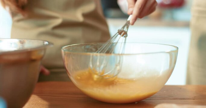 Close up of school age girl learning to whip cream in glass bowl. Mom takes corolla from her daughter and continues to stir yolks.