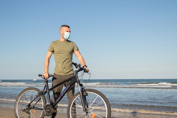 Boy with green shirt and mask arriving at his destination after a bike ride to rest on the beach