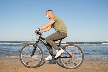 Fototapeta na wymiar Boy with green t-shirt and mask walking along the beach on his bike