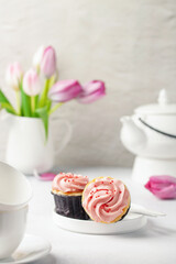 Cupcakes, tulips and white utensils for a tea ceremony on a bright background. Holiday concept