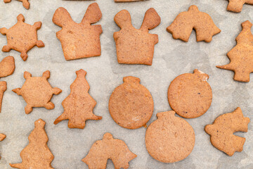 Baked gingerbread cookies in various shapes without decorations, lying on baking paper, top view.