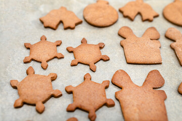Baked gingerbread cookies in various shapes without decorations, lying on baking paper.