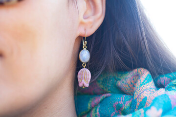 Detail of female ear wearing moon stone mineral floral shape bead earring