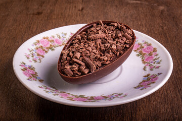 Mini stuffed chocolate easter egg with grated chocolate on the top on a white plate with flowers design on a wooden table.
