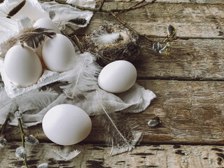 Natural easter eggs, feathers, willow branches, nest on rustic aged wooden table. Rural still life