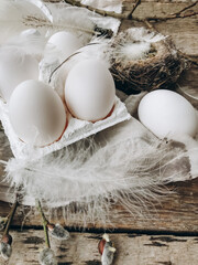 Natural easter eggs, feathers, willow branches, nest on rustic aged wooden table. Rural still life