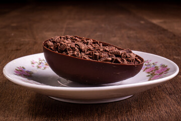 Mini stuffed chocolate easter egg with grated chocolate on the top on a white plate with flowers design on a wooden table.