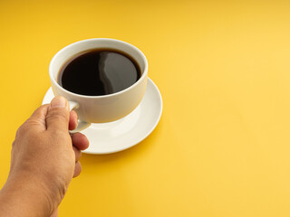 Close-up of a hand holding a white coffee cup with a yellow background. Space for text. Concept of beverage and relaxation