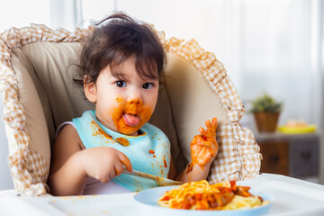 Adorable little toddler girl or infant baby eating delicious spaghetti food with dirty mouth Funny...