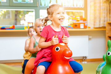 Little girls riding on play horses in kindergarten