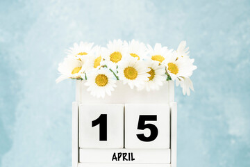 cube calendar for April with daisy flowers over blue with copy space