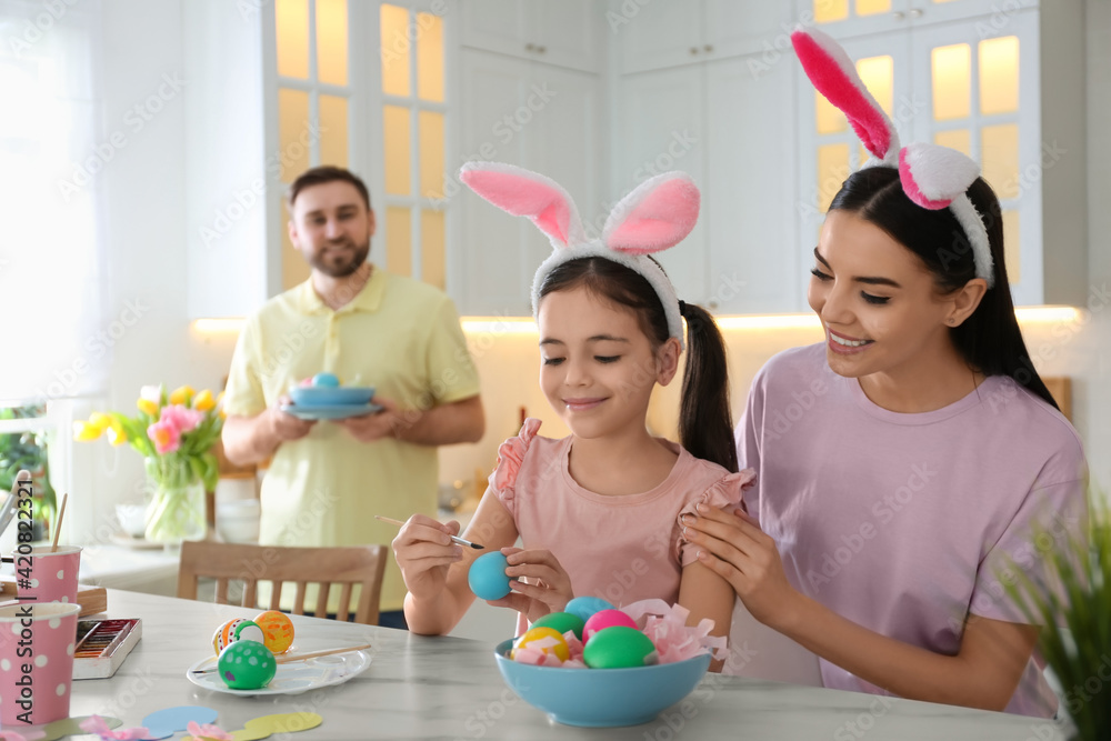 Poster Happy family painting Easter eggs at table indoors