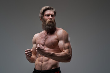 Angry bodybuilder with fists looks away in gray background