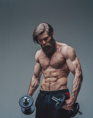 Fototapeta na wymiar Strong bodybuilder with dumbells and naked torso posing in studio
