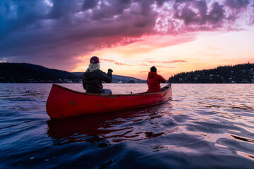 Couple friends on a wooden canoe are paddling in water. Dramatic Sunset Sky Art Render. Taken in...