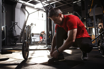 Obraz premium Male athlete tying shoelaces at the gym, copy space