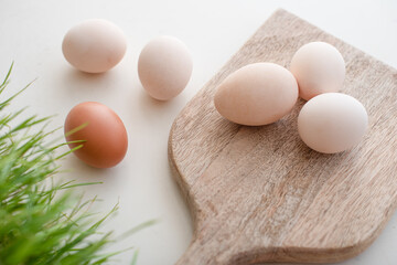 white and brown eggs lie next to greens on a wooden board on a white table. home life. The process of preparing for Easter.