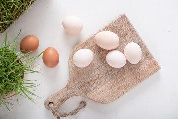 white and brown eggs lie next to greens on a wooden board on a white table. home life. The process of preparing for Easter.