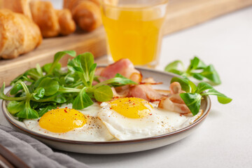Continental breakfast - fried eggs, bacon and lettuce leaves in a plate on a bright background. Top View