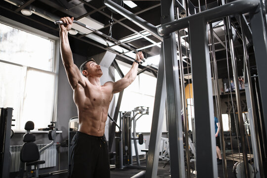 Low angle shot of a ripped strong male bodybuilder exercising on lat pull down gym machine