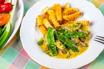 Roasted liver in curry sauce with green sweet pea pod and french fries.