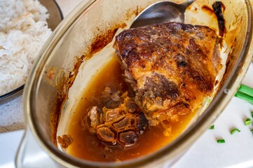 Baked pork neck meat in glass pan with onion, rice in plate.