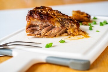 Piece of freshly baked juicy pork neck meat, garlic and fork on board.