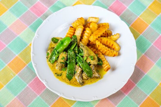 Roasted liver in curry sauce with green sweet pea pod and french fries.