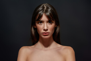 Fototapeta premium Beauty portrait of naked young brunette woman with big brown eyes and colorful makeup looking at camera, posing isolated over black background