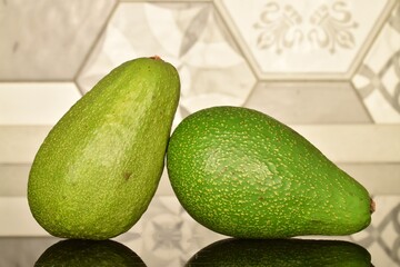 Two ripe organic avocados, close-up, on a tile background.