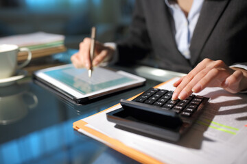 Businesswoman hands using tablet and calculator in the night