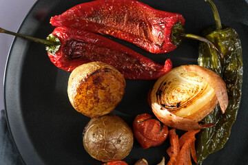 Roasted red capia pepper, garlic, cherry tomato and green pepper on a black porcelain plate. Delicious baked vegetables.